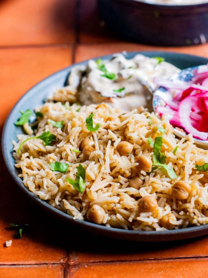 a plate of chana pulao with raita and pickled onions