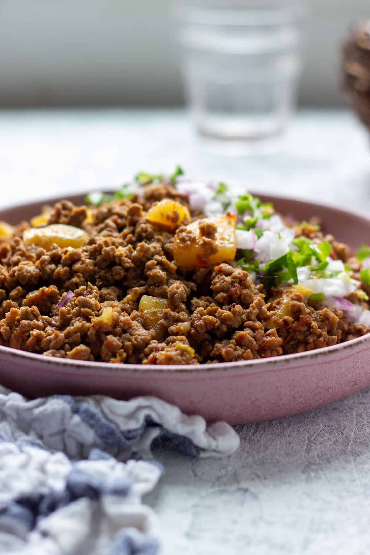 Aloo Qeema i a dish garnished with onions and cilantro 