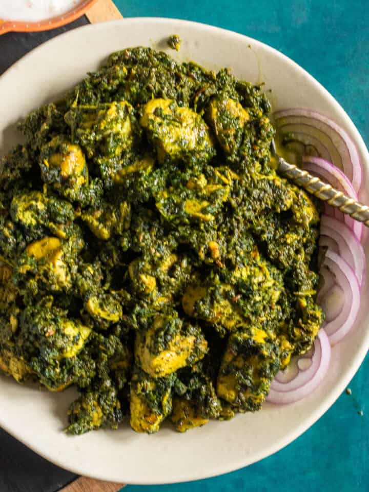 A dish of Palak Chicken garnished with red onions