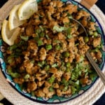 Top down view of a bowl of chicken keema garnished with cilantro and pieces of lemon.