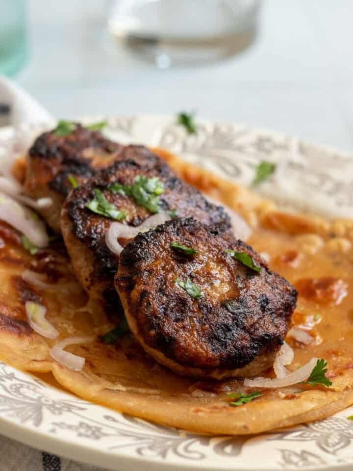 ¾ side view of three chicken kababs on top of a paratha