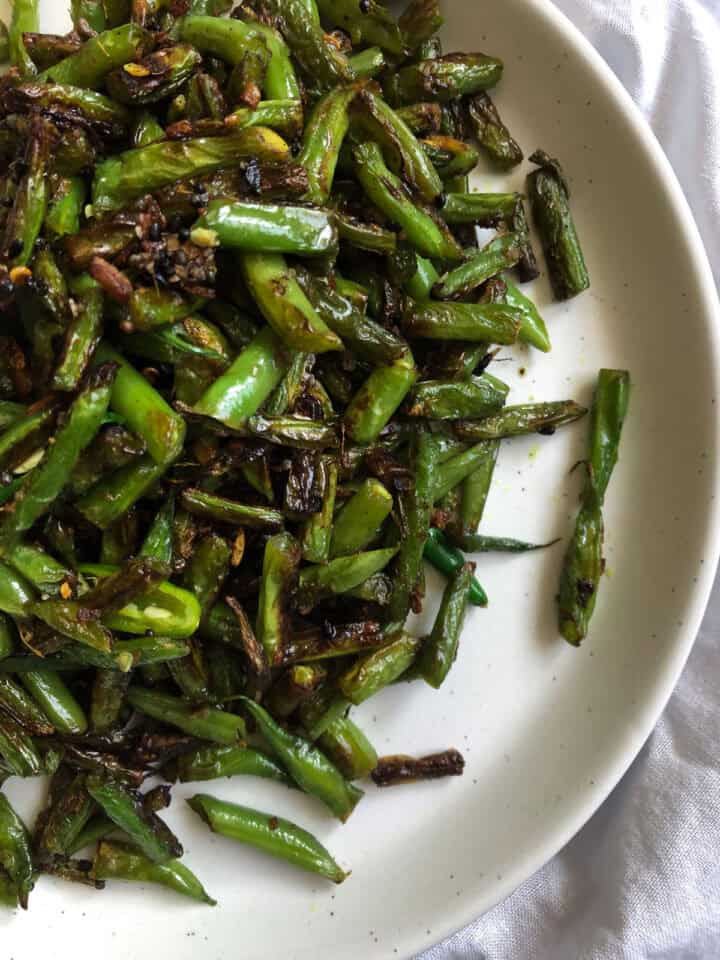 a white plate with lightly charred green beans