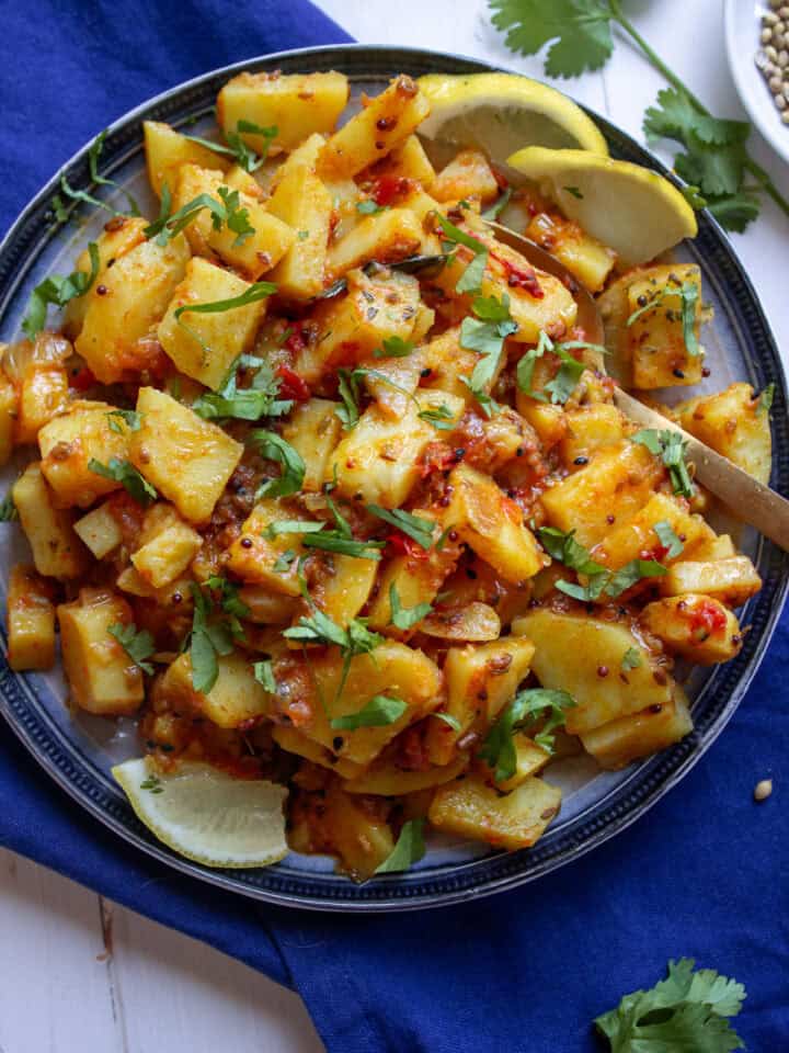 A top down shot of a plate of achari aloo, roti in the corner