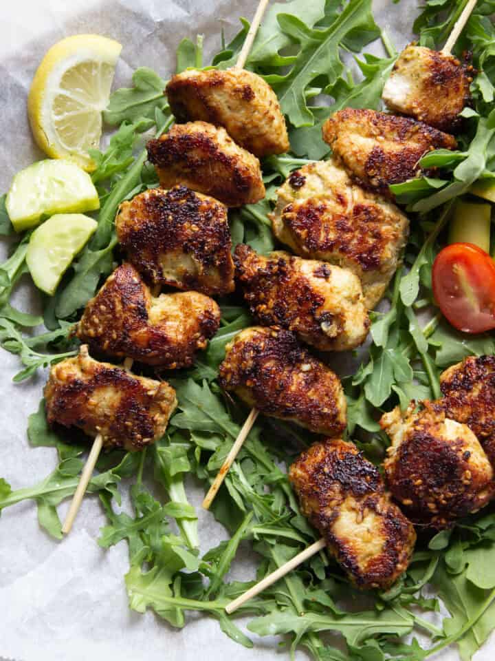 Three Sesame Ginger Chicken skewers on a bed of arugula