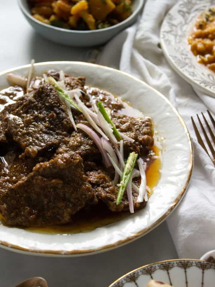 a plate with pasanday garnished with onions and chilies, two bowls of food in the background