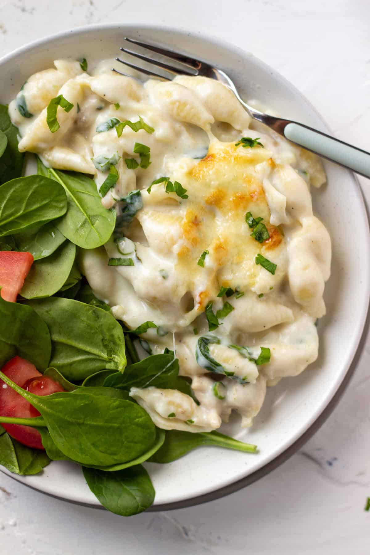 a plate with a spinach salad and white sauce pasta