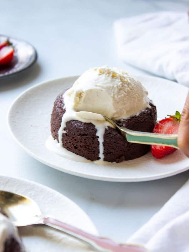 A plate with a lava cake, half a strawberry and melting vanilla ice cream