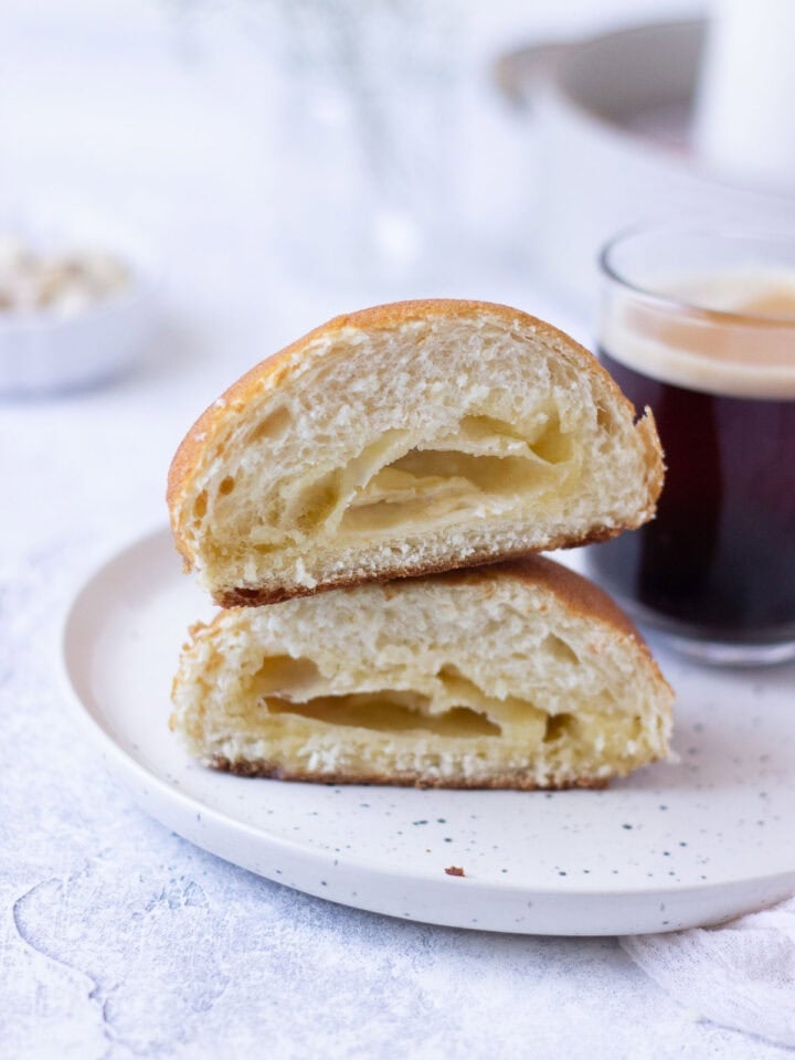 Papaproti Bun halved and on a plate with a cup of coffee. Melted butter centre.