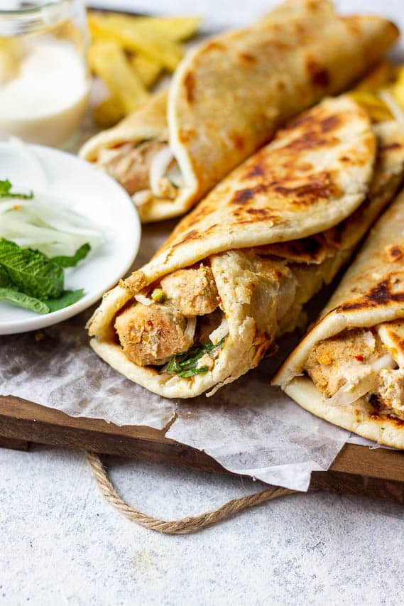 Partial view of chicken paratha roll on a wooden tray. partial of mint and onions.