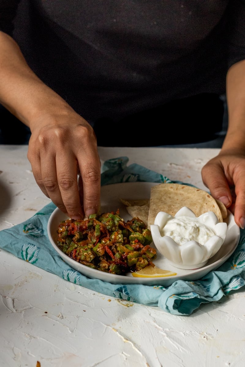 Bhindi Maslaa being eaten with a roti. A roti and a bowl of yoghurt on the plate. 