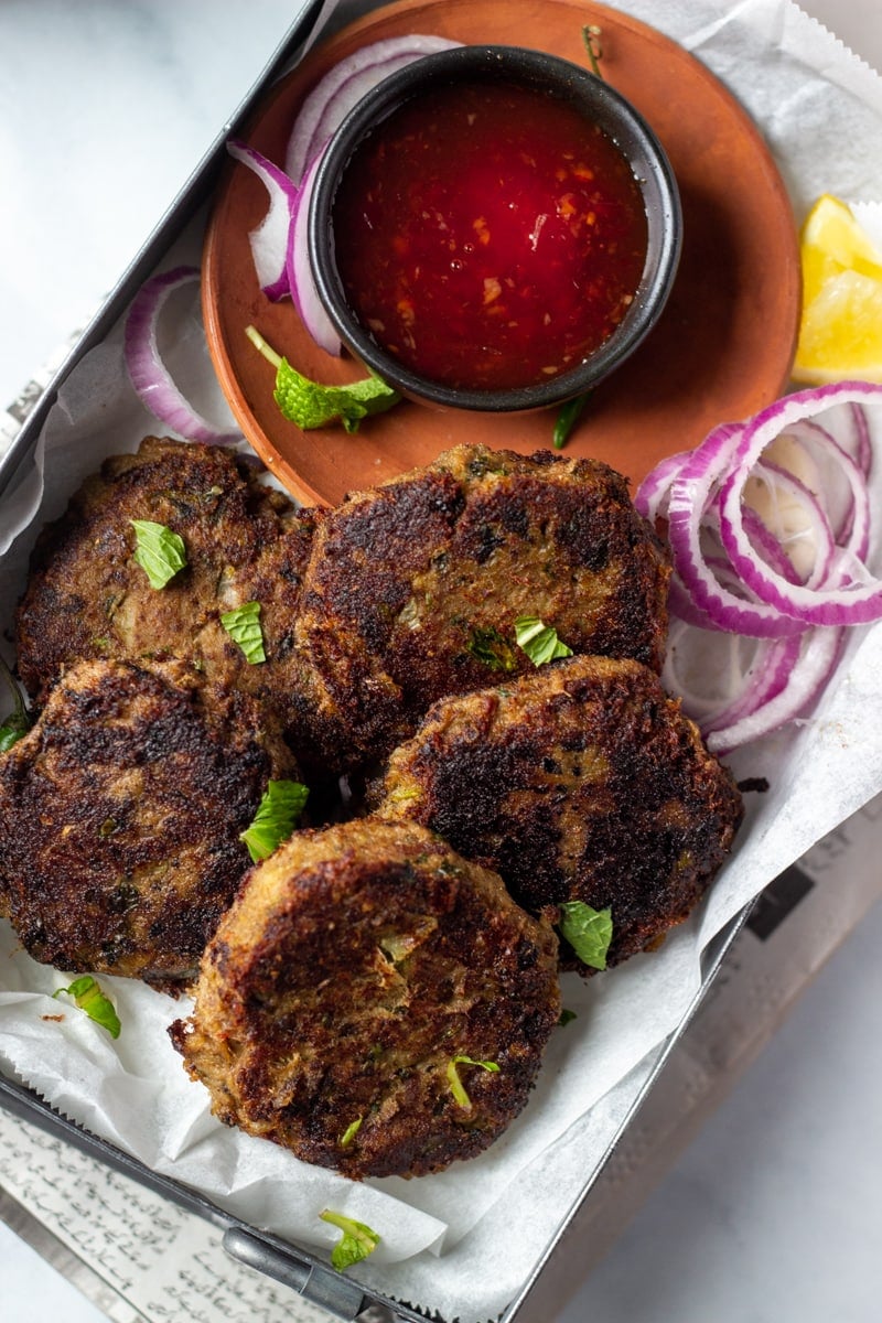 top down view of a dish with shami kabab, hot sauce, and red onion rings