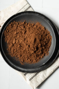 A black plate filled with a mound of Garam Masala sits on a sheet of newspaper against a white tiled background.