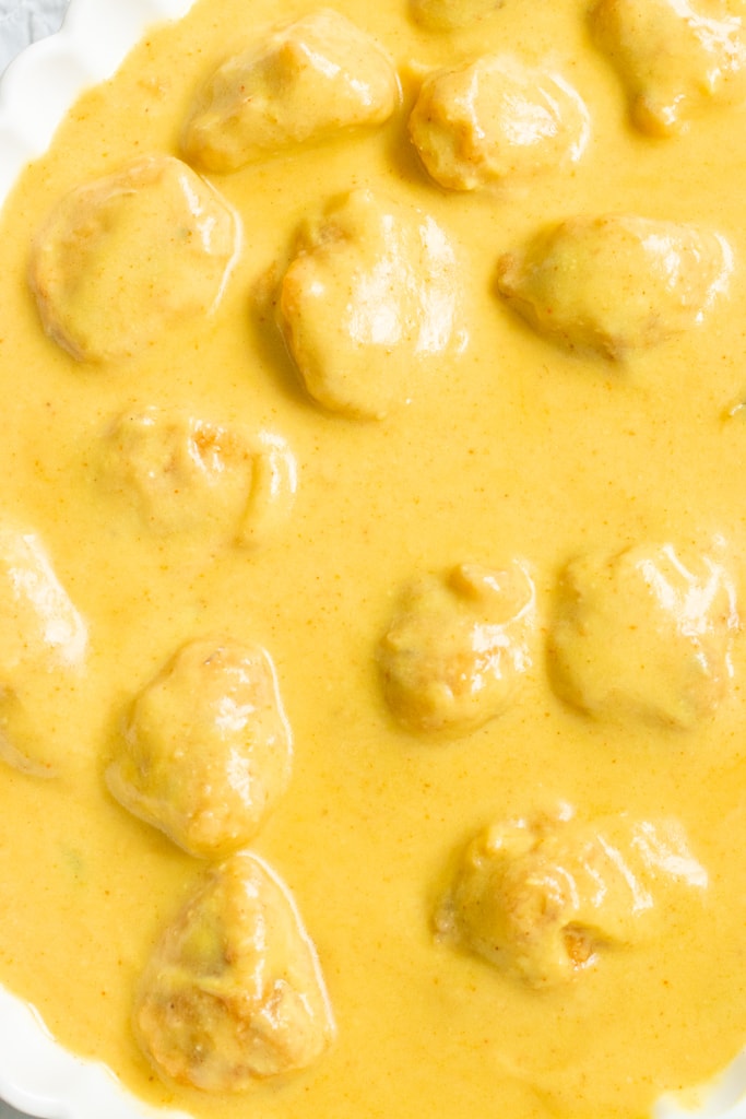 Creamy golden Karhi sauce with chunks of chicken in a white dish, viewed from above.