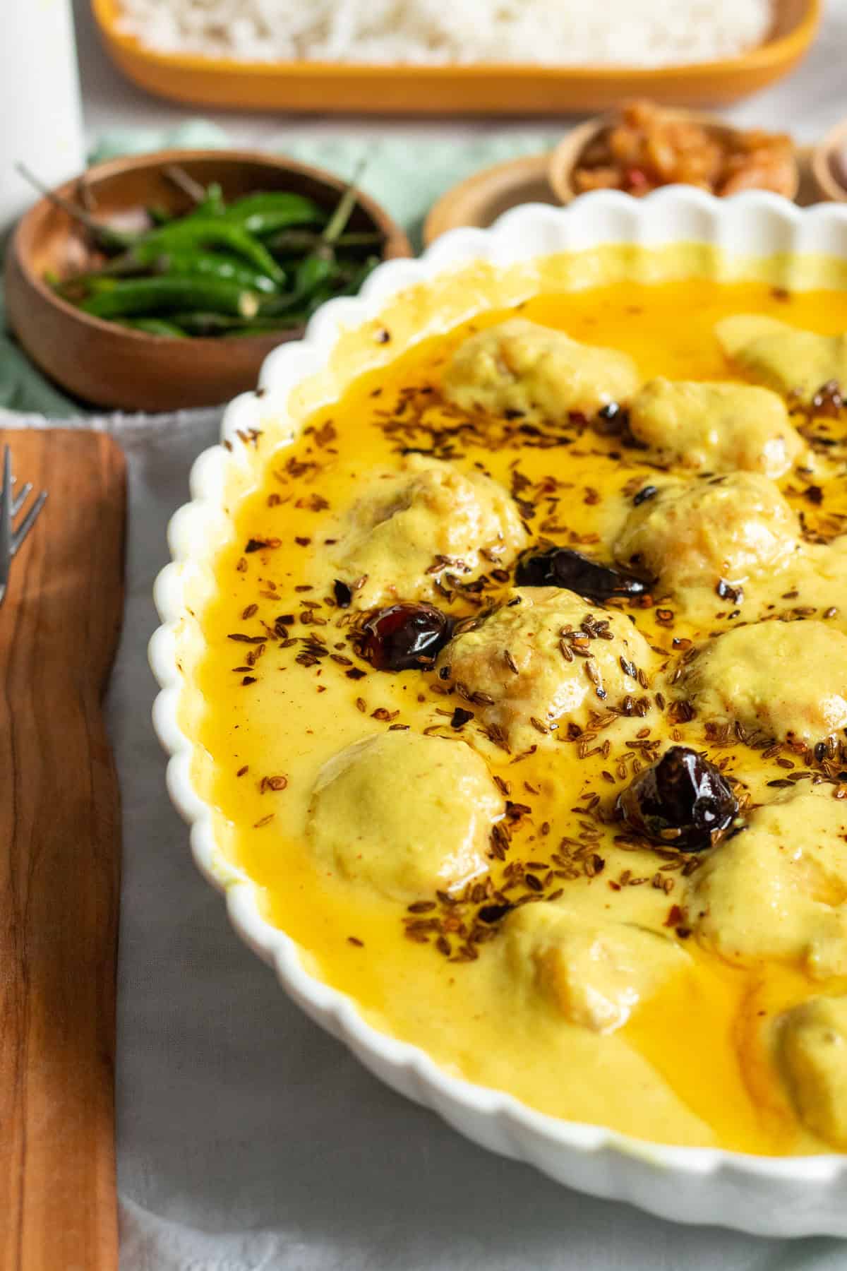 a karhi pakora dish, green chilies in a bowl, white rice in a dish