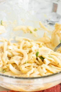 A close-up of a glass bowl filled with creamy coleslaw made of sliced cabbage and green peppers, coated in a mayonnaise-based dressing—perfect as a crunchy side or even as inspiration for How to Make Pakoras with a twist. A metal fork rests in the mixture.