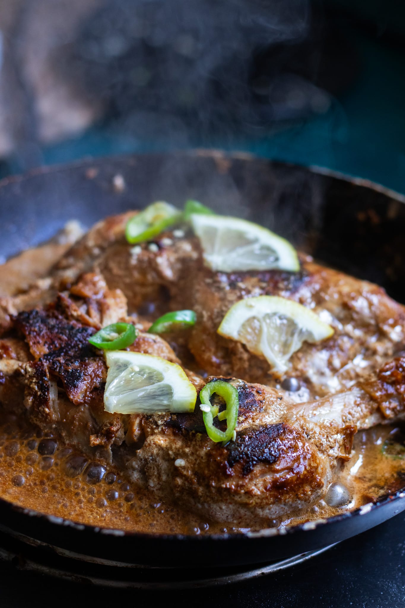 two pieces of tawa chicken in a pan, smoke rising from the chicken 