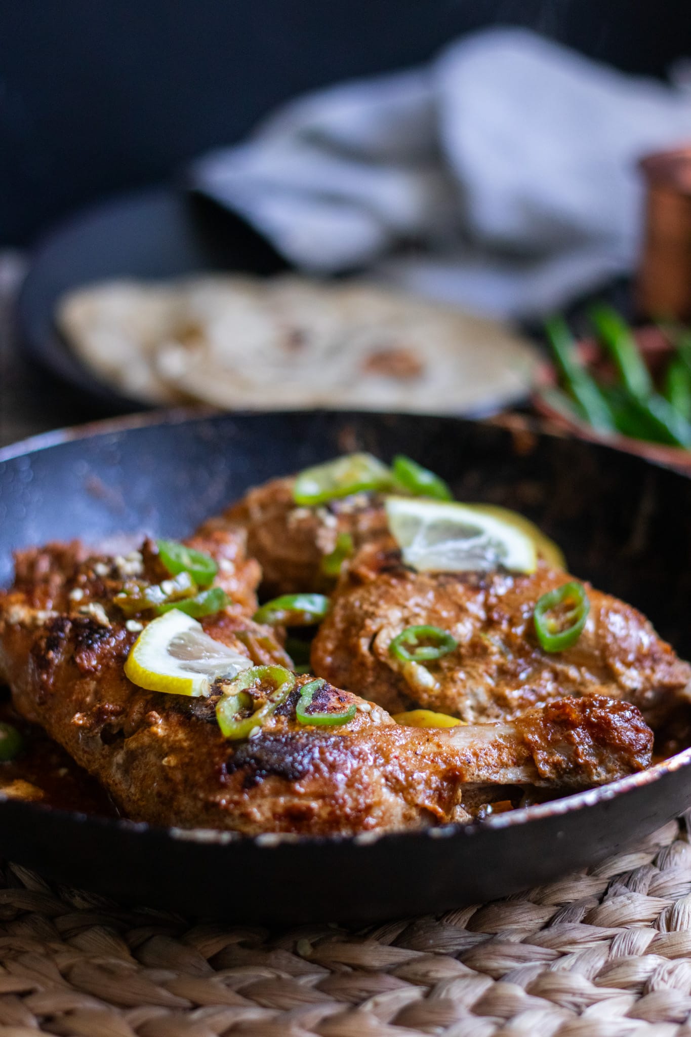 two cooked pieces of tawa chicken in a pan, roti in the backrgound