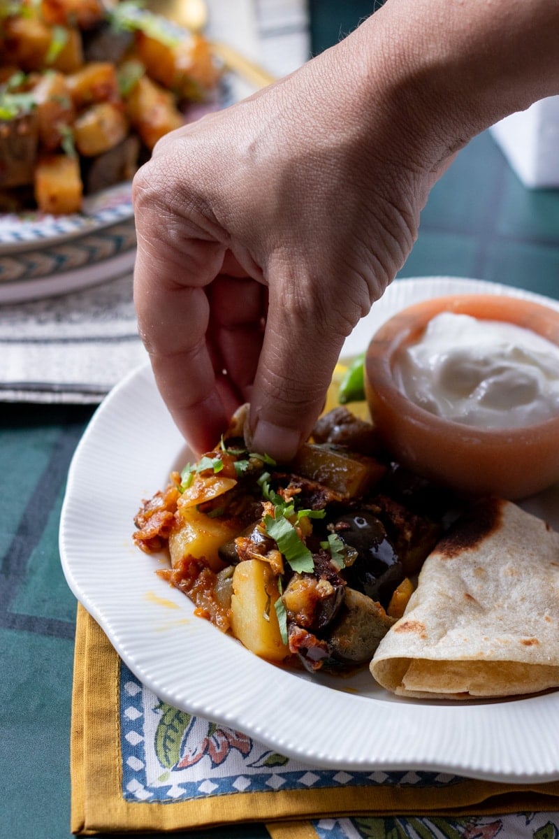 a hand making a niwala of aloo baingan with chapati 