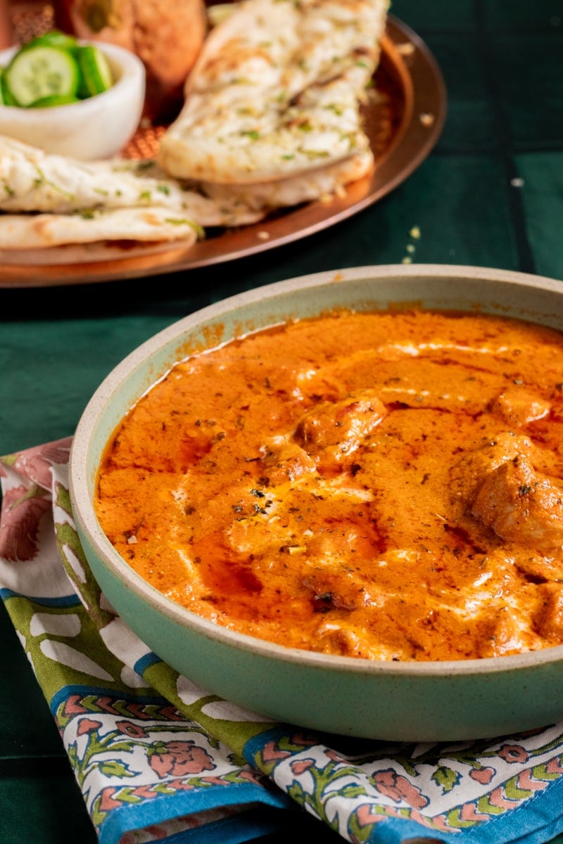 ¾ view of a dish of chicken handi, plate with naan in background