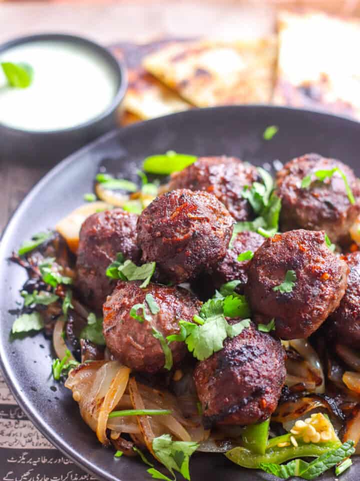Gola Kabab on a plate with cilantro and a bowl of chutney raita in the background