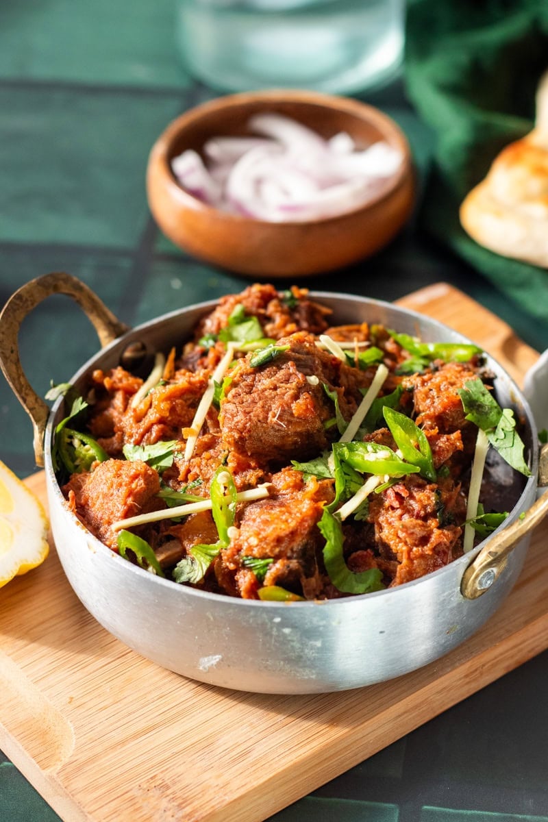 karahi gosht bowl on a wooden board, naan and onions in the background 