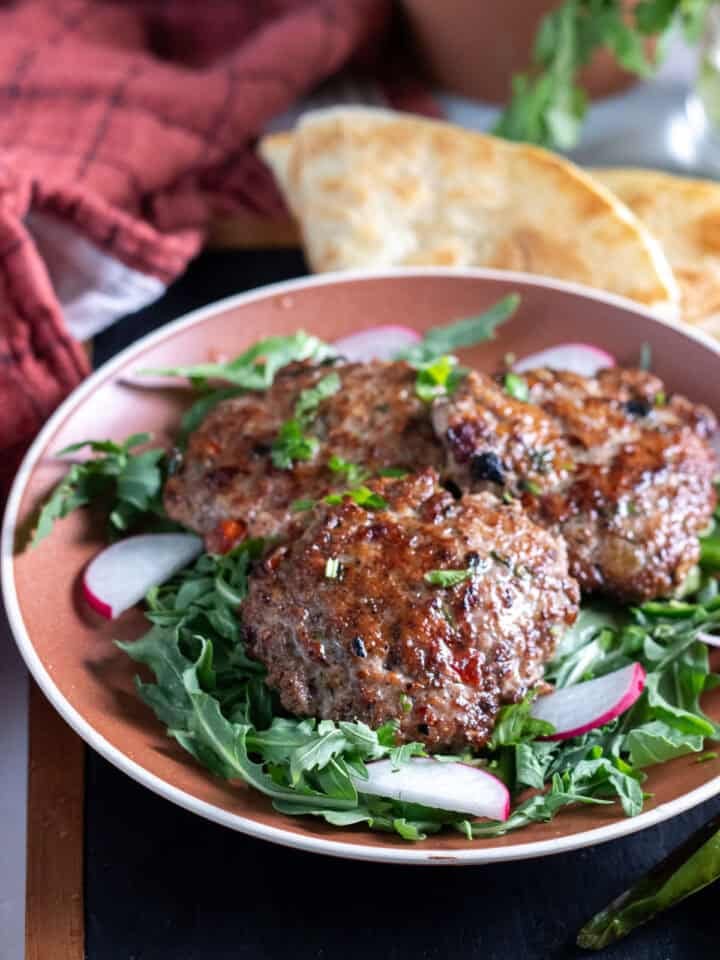 chicken chapli kabab on a bed or arugula, paratha in the back