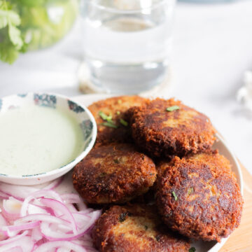 a plate of shami kabab with onions, a green raita/chutney and cilantro in a jar in the background