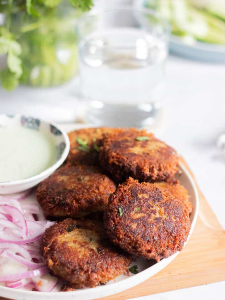 a plate of chicken shami kababs with chutney and onnions and glasses of water