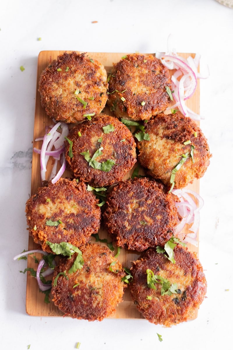 top down view of a wooden tray of cooked chicken shami kababs garnished with cilantro and onions 