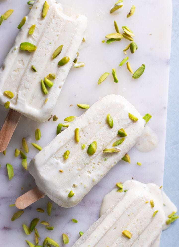 pista kulfi on a marble board with pistachios scattered over top